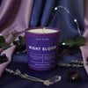 Purple candle labeled 'Night Bloom' on a decorative fabric background with flowers and leaves.